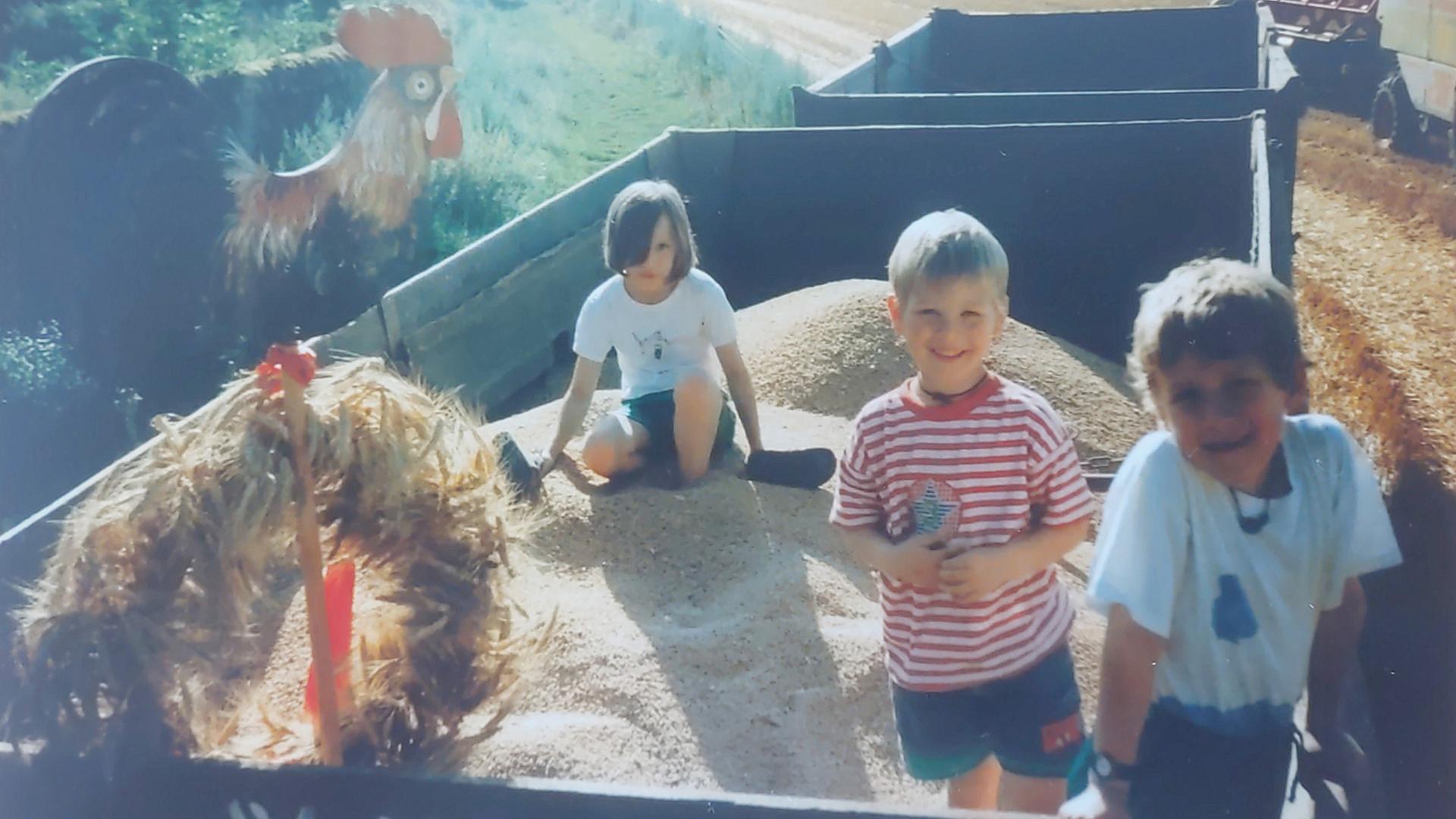 Kinder auf einem Getreideanhänger in einem Bauernhof.