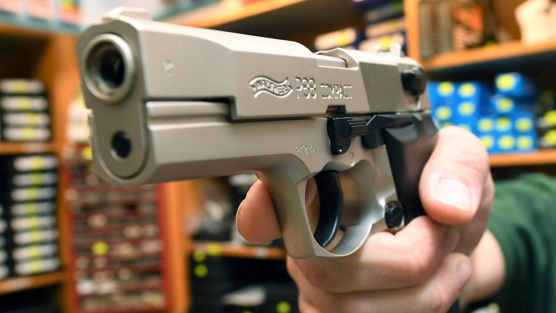 Ein Verkäufer hält in einem Waffengeschäft eine Pistole in der Hand. 