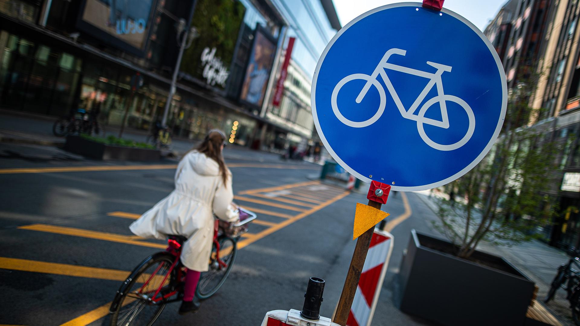 In der Friedrichstraße in Berlin fährt eine Frau mit dem Rad. Rechts steht ein rundes, blaues Schild mit einem Fahrradsymbol in der Mitte. In der Friedrichstraße in Berlin fährt eine Frau mit dem Rad. Rechts steht ein rundes, blaues Schild mit einem Fahrradsymbol in der Mitte.