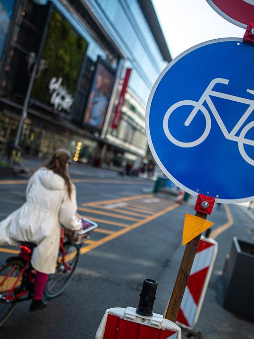 In der Friedrichstraße in Berlin fährt eine Frau mit dem Rad. Rechts steht ein rundes, blaues Schild mit einem Fahrradsymbol in der Mitte.