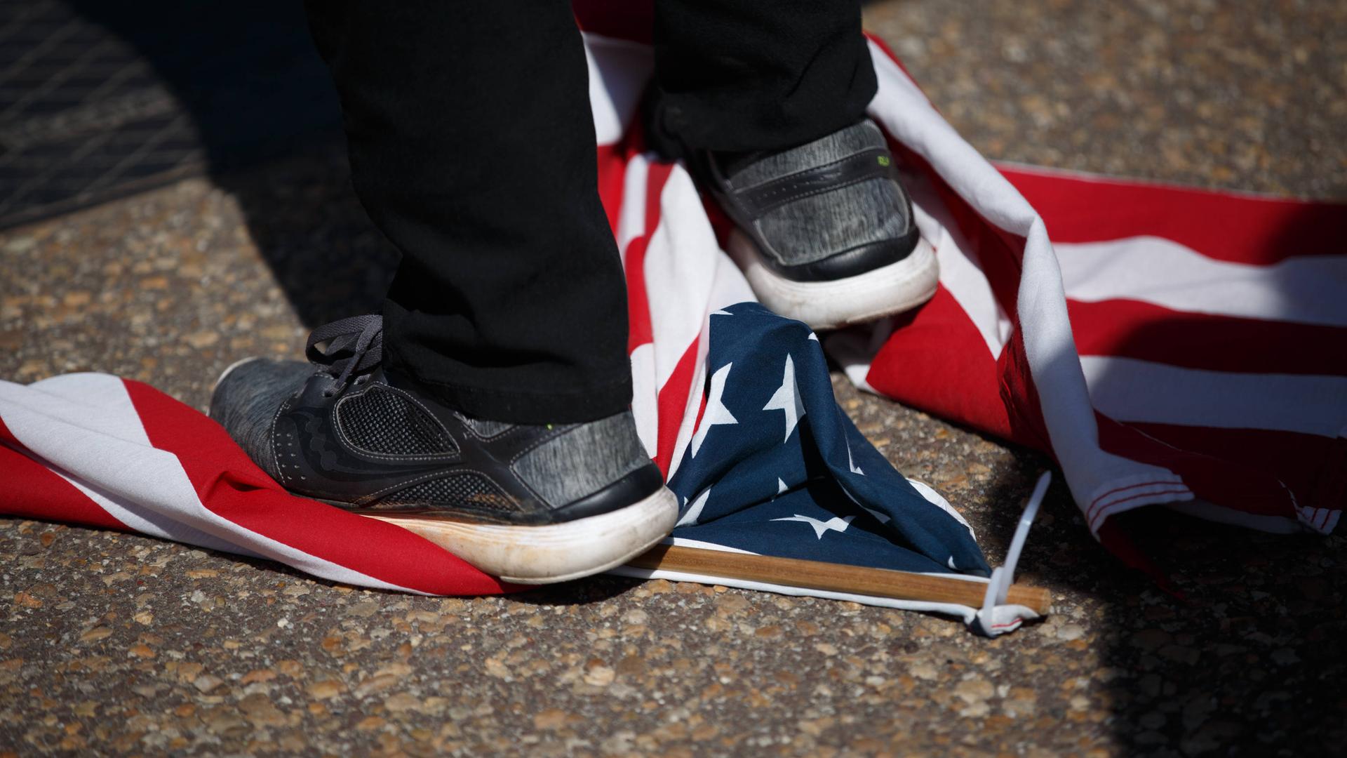 Großaufnahme eines Fußes, der auf einer am Boden liegenden us-amerikanischen Flagge steht. Großaufnahme eines Fußes, der auf einer am Boden liegenden us-amerikanischen Flagge steht.