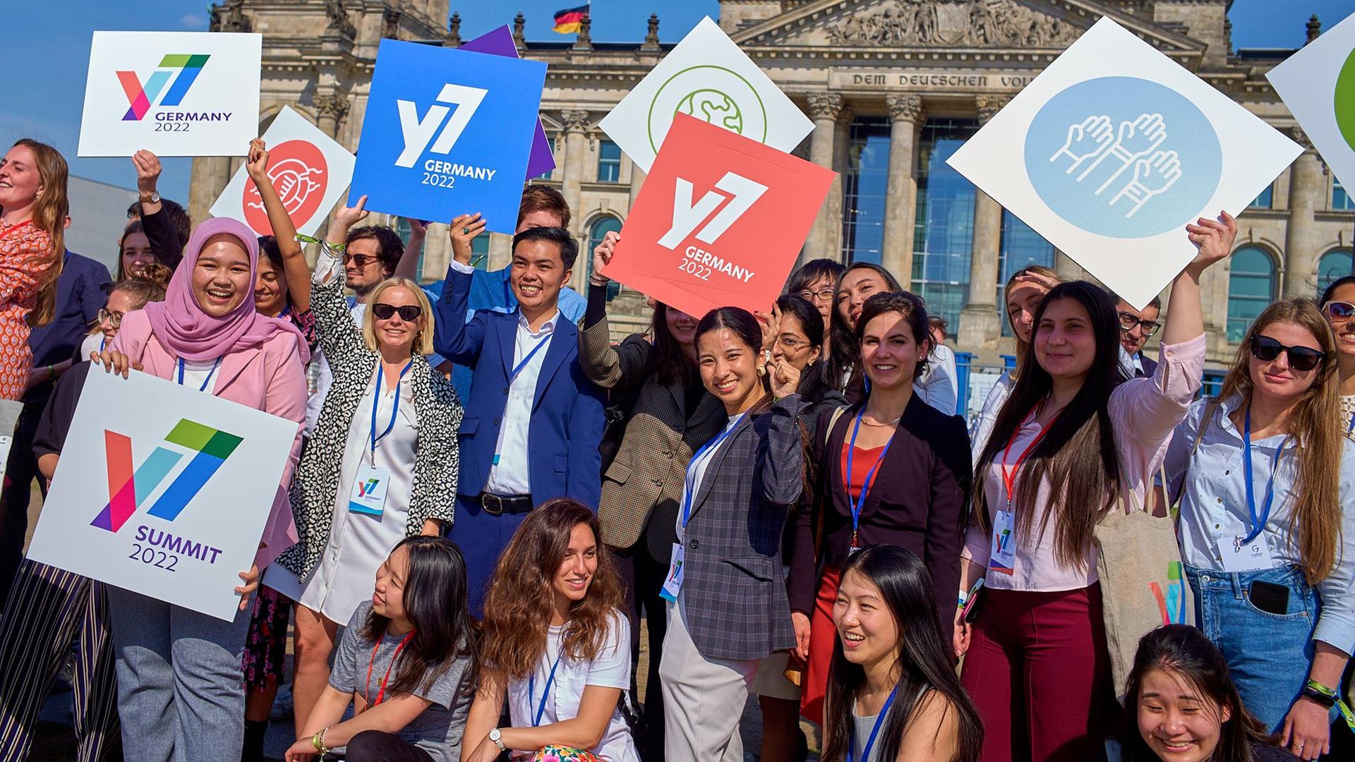 Teilnehmer des Jugendgipfels Y7 stehen vor dem Reichstagsgebäude in Berlin. Sie halten zum Teil Schilder in die Luft mit dem Logo des Gipfels und anderen Symbolen. Teilnehmer des Jugendgipfels Y7 stehen vor dem Reichstagsgebäude in Berlin. Sie halten zum Teil Schilder in die Luft mit dem Logo des Gipfels und anderen Symbolen.