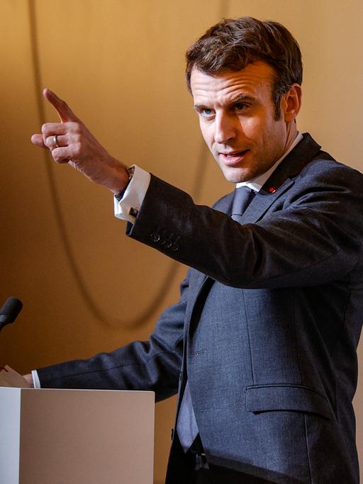Emmanuel Macron spricht an einem Rednerpult und streckt den Zeigefinger in einer zukunftsweisenden Geste in die Luft.