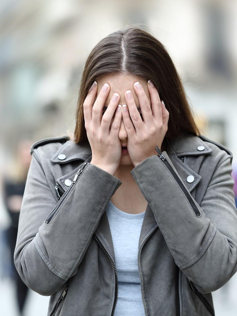 Eine Frau versteckt ihr Gesicht hinter ihren Händen. Der Hintergrund hinter ihr ist verschwommen.