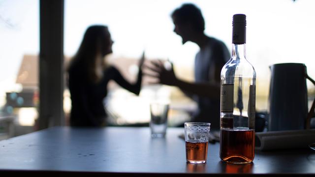 Im Hintergrund (unscharf) streitet sich ein Paar, im Vordergrund steht Alkohol auf einem Tisch, Symbolbild