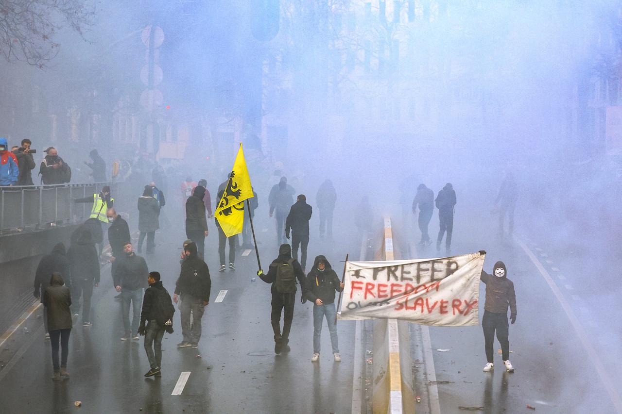Zum Teil maskierte Personen stehen im Tränengas. Zwei von ihnen halten ein Plakat mit der Aufschrift "Prefer freedom over slavery". Zum Teil maskierte Personen stehen im Tränengas. Zwei von ihnen halten ein Plakat mit der Aufschrift "Prefer freedom over slavery".