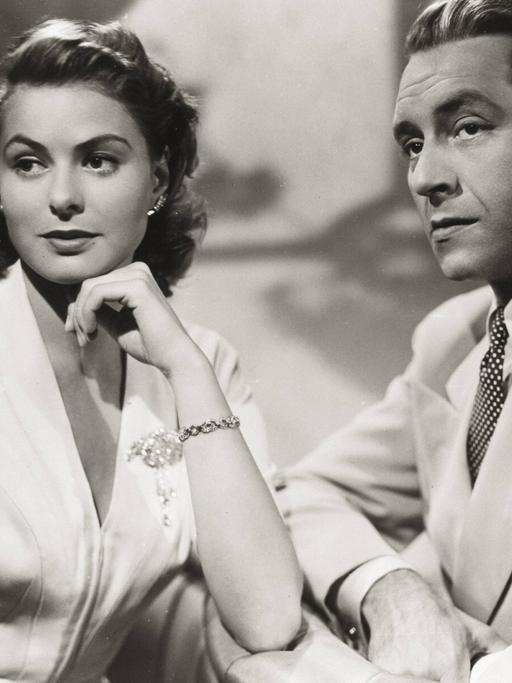 Historisches Schwarzweißfoto von Ingrid Bergman und Paul Henreid, die mit ernstem Blick nebeneinander sitzen.