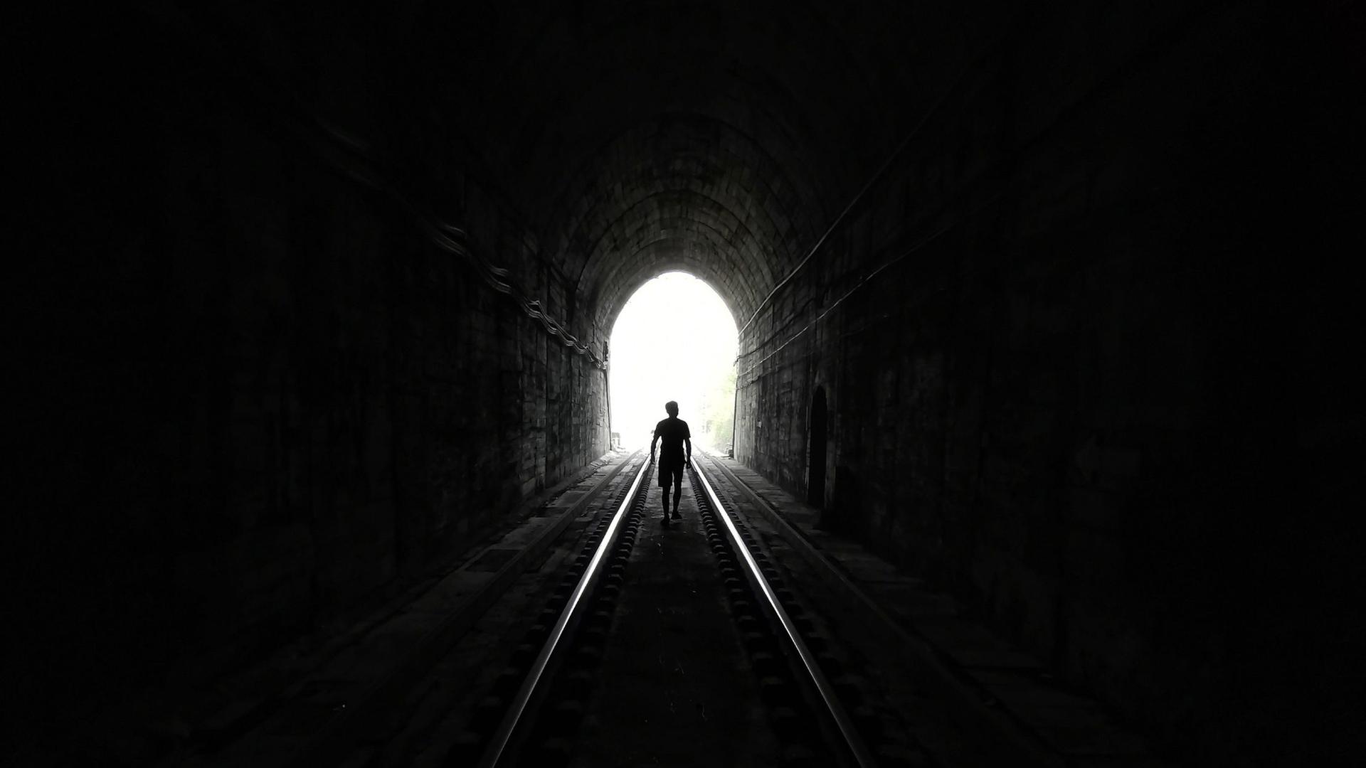 Eine Person läuft auf das Licht am Ende eines Tunnels zu. Eine Person läuft auf das Licht am Ende eines Tunnels zu.