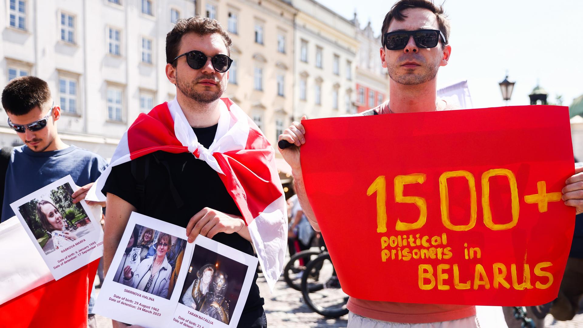 Zwei junge Männer halten Bilder von politischen Gefangenen und ein Banner in der Hand, das angeblich auf mehr als 1.500 politische Gefangene in Weißrussland verweist.