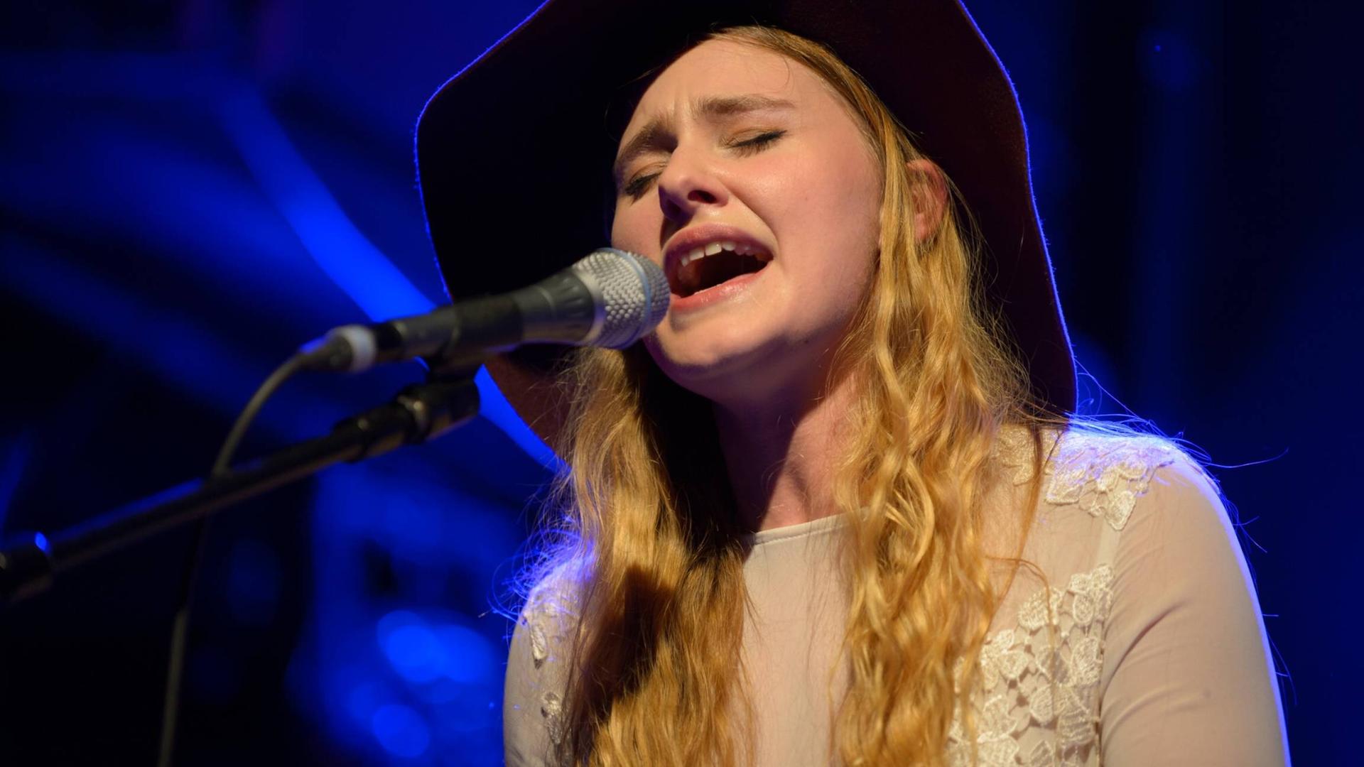 Die Sängerin Mia Diekow hat die Augen geschlossen und singt in in Mikrofon - sie trägt einen schwarzen Cowboy-Hut. Die Sängerin Mia Diekow hat die Augen geschlossen und singt in in Mikrofon - sie trägt einen schwarzen Cowboy-Hut.