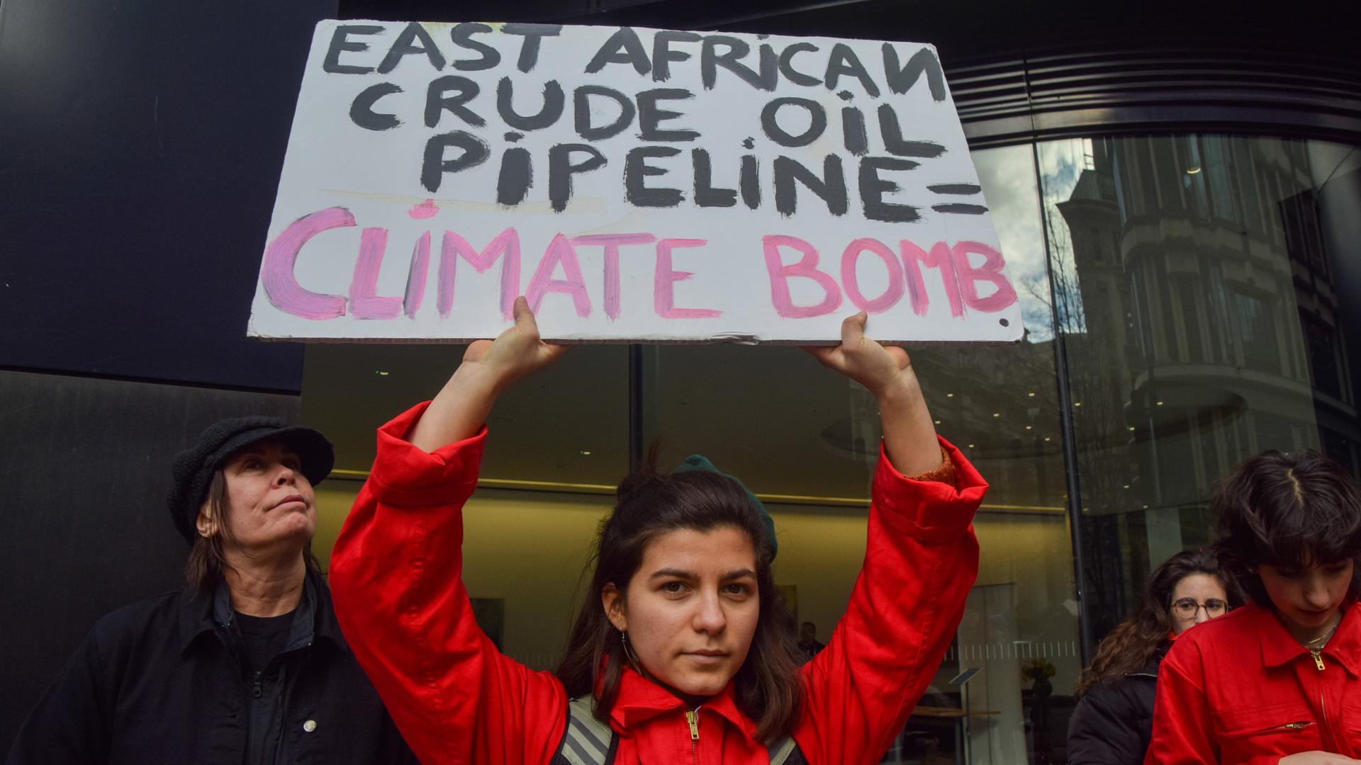 Eine junge Frau hält in London ein Schild in der Hand auf dem steht: "East African Crude Oil Pipeline = Climate Bomb". 