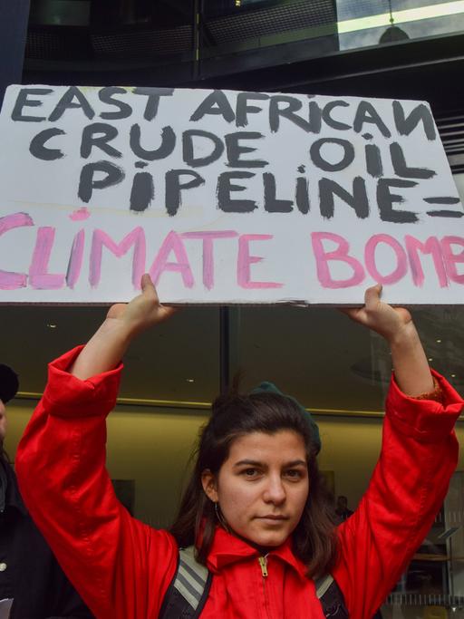 Eine junge Frau hält in London ein Schild in der Hand auf dem steht: "East African Crude Oil Pipeline = Climate Bomb". 