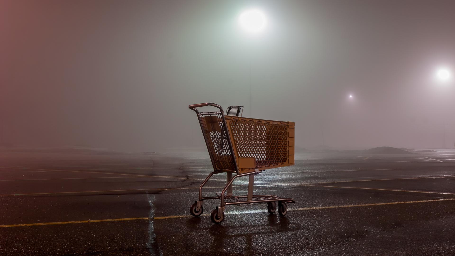 Ein leerer Einkaufswagen auf einem Parkplatz in der Dunkelheit.