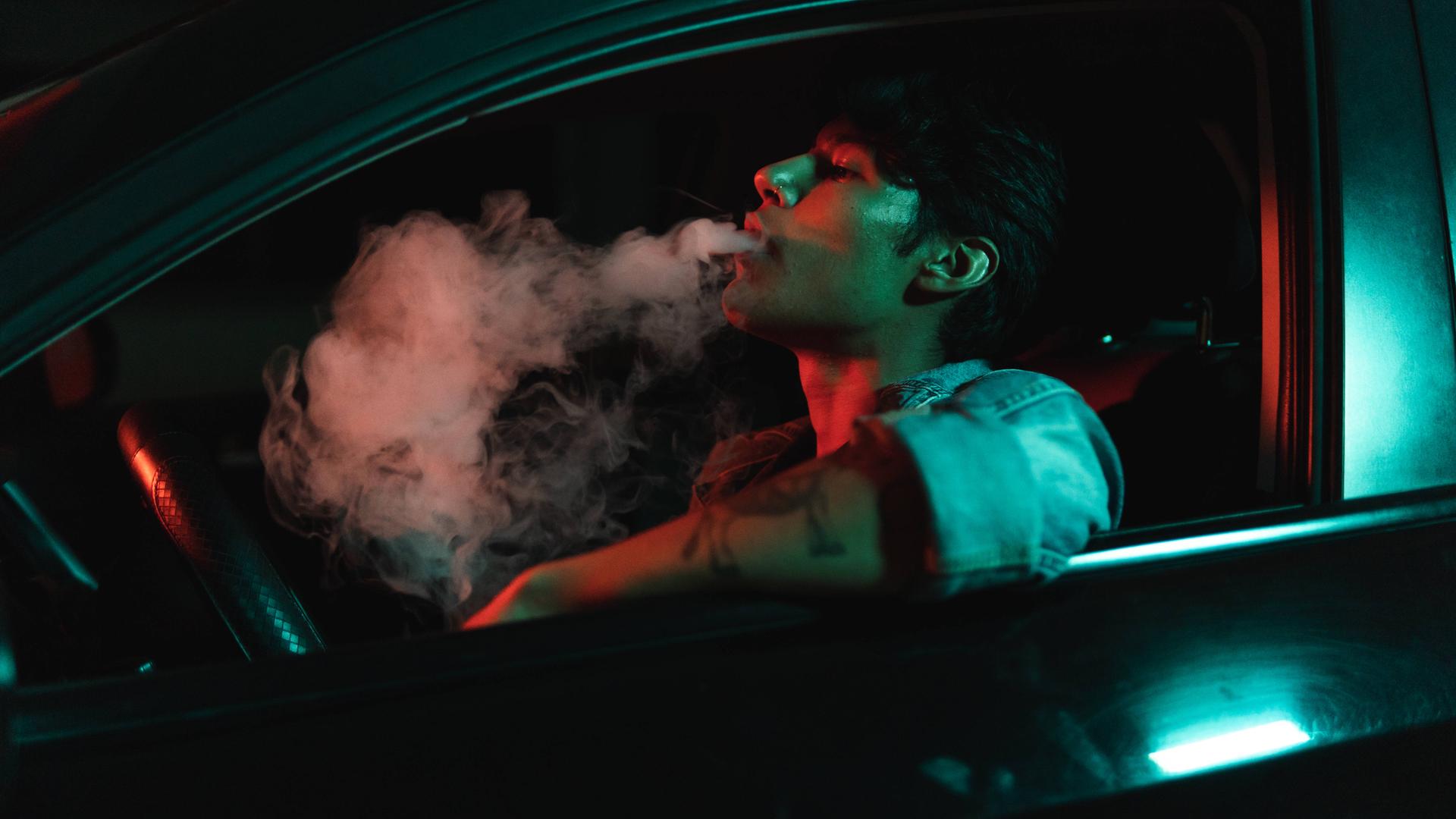 Ein junger Mann sitzt nachts in einem Auto und raucht.
