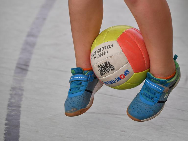 Ein Schulkind hüpft mit einem Ball zwischen den Beinen.