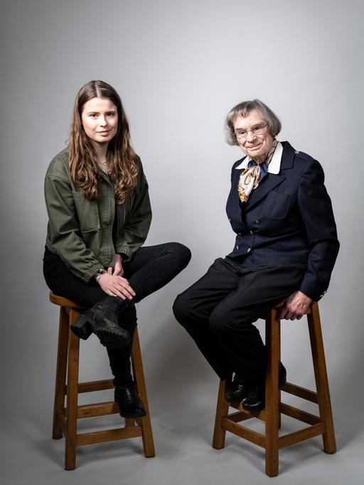 Das Bild zeigt die junge Klimaaktivistin Luisa Neubauer  mit langen braunen Haaren und ihre Großmutter Dagmar Reemtsma mit kurzer Pagenkopf-Frisur. Beide sitzen vor einem hellgrauen Hintergrund auf hohen Barhockern und schauen in die Kamera.