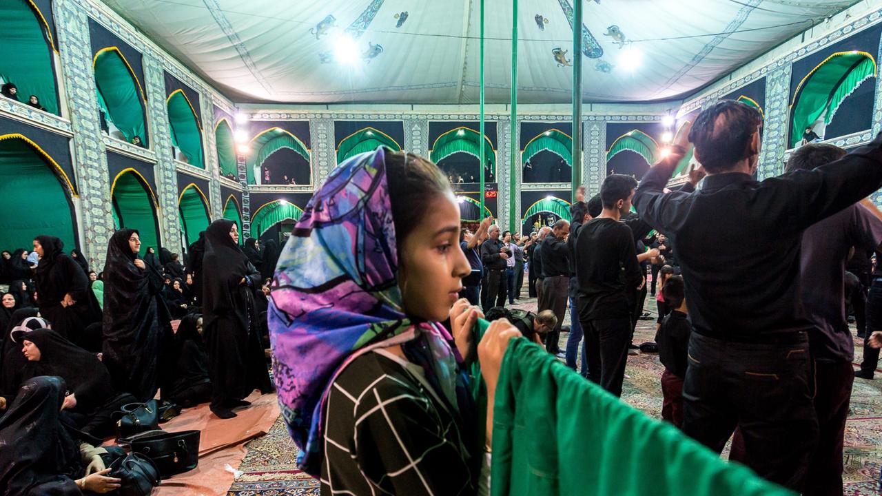 Ein iranisches Mädchen beobachtet vom Frauenbereich einer Moschee wie die die Männer beten 