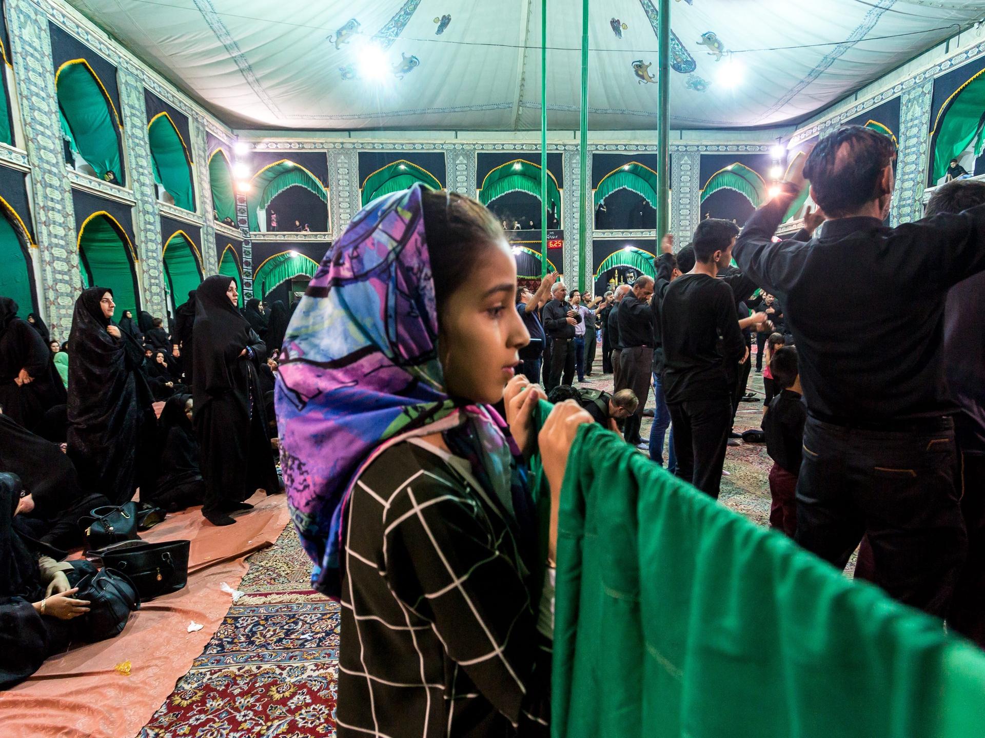 Ein iranisches Mädchen beobachtet vom Frauenbereich einer Moschee wie die die Männer beten 