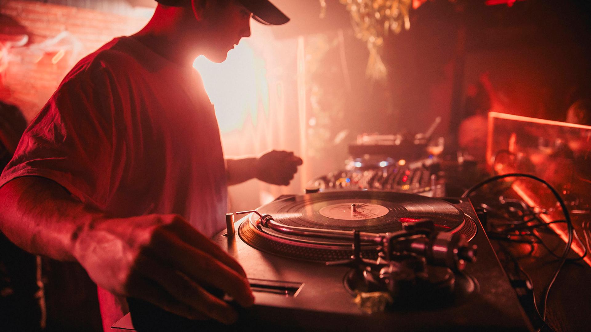 Ein DJ steht in einem Club an einem Plattenspieler.