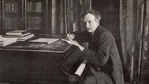 Ein Mann sitzt vor einem Klavier und schreibt Noten auf ein Blatt Papier. Es ist der Komponist Richard Strauss. 
