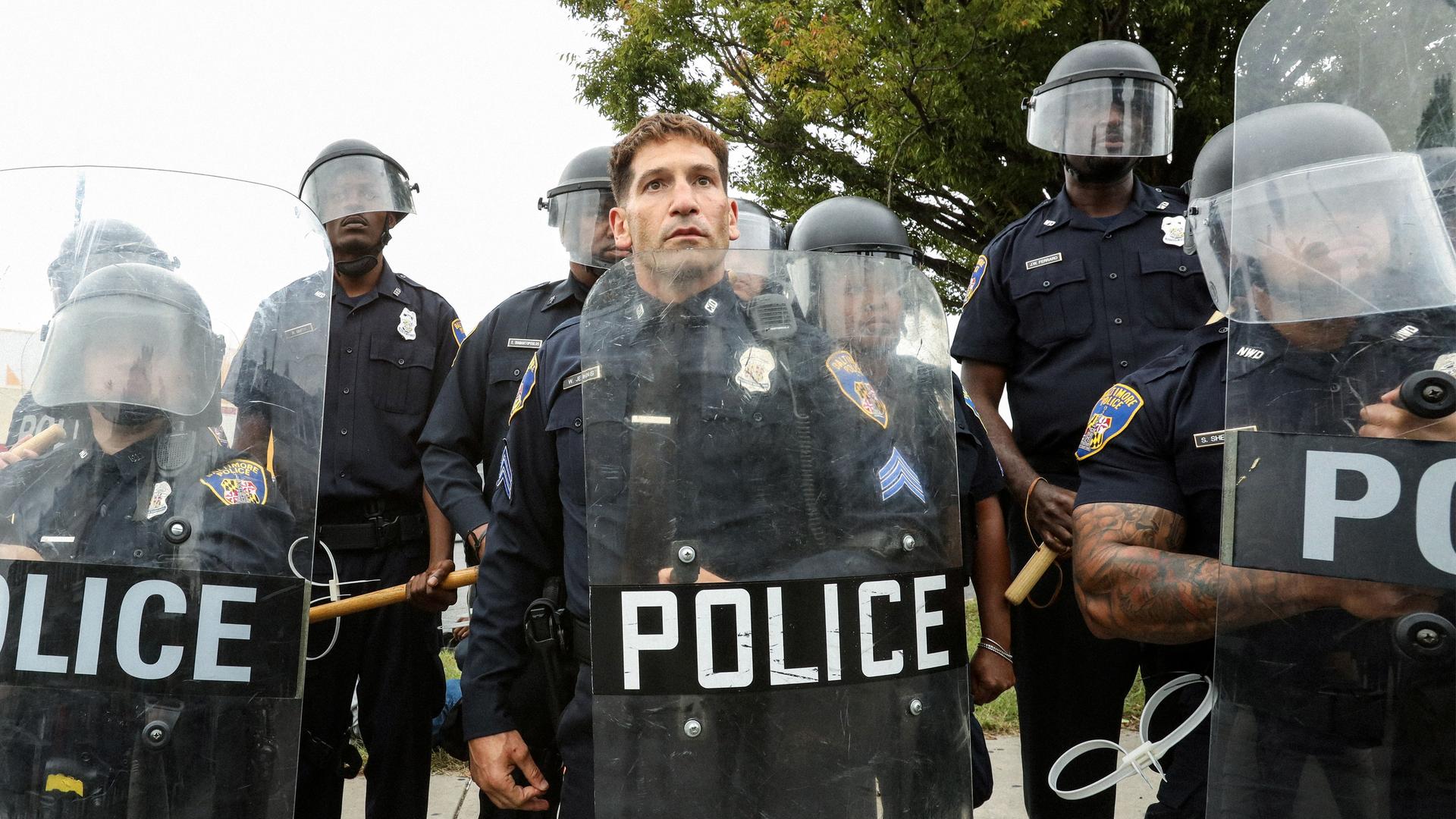 Polizisten stehen mit Helmen, Schlagstöcken und Schildern in einer Reihe.