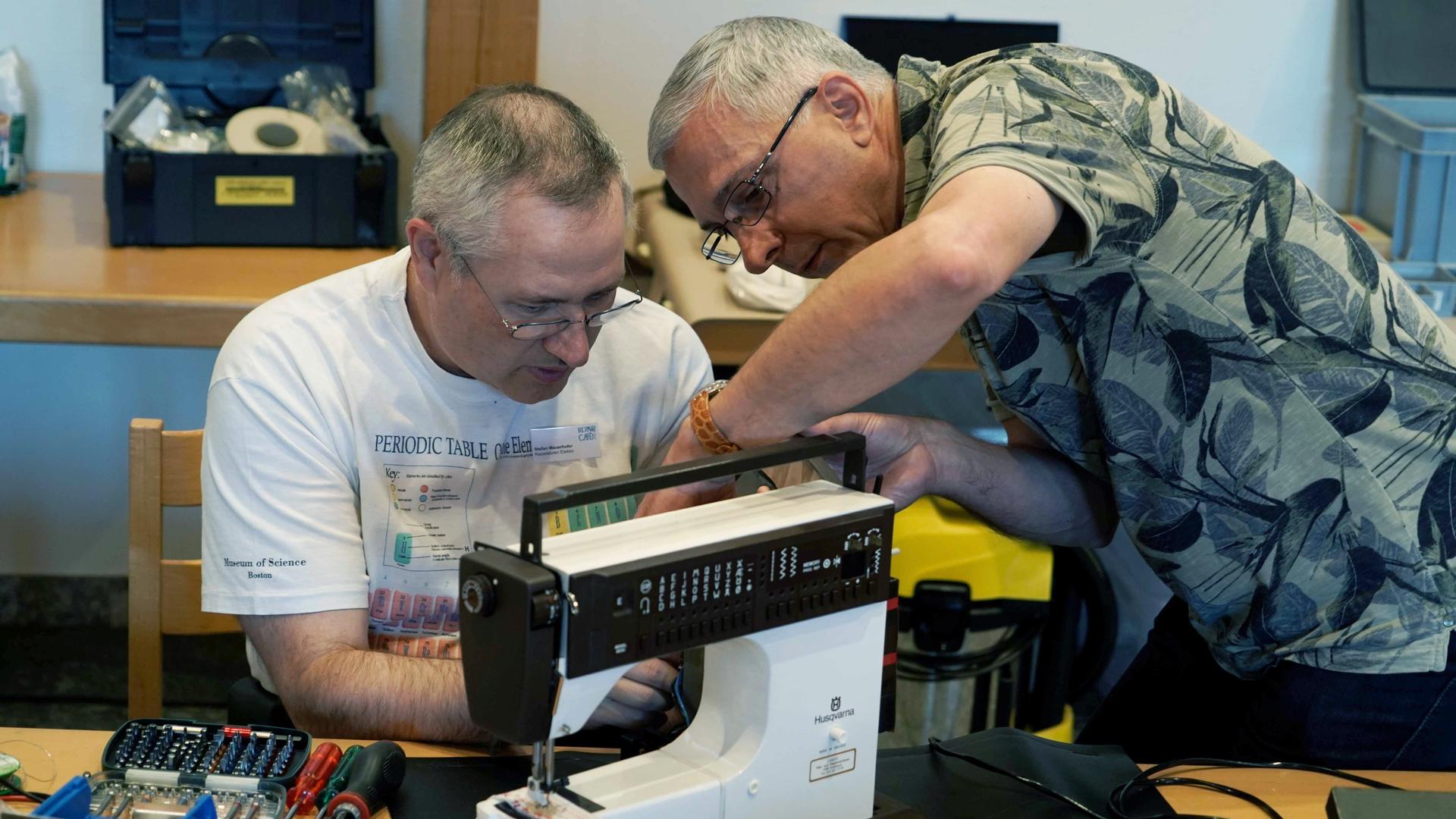 Zwei Mitarbeiter eines Repair-Cafes reparieren eine Nähmaschine. Zwei Mitarbeiter eines Repair-Cafes reparieren eine Nähmaschine.