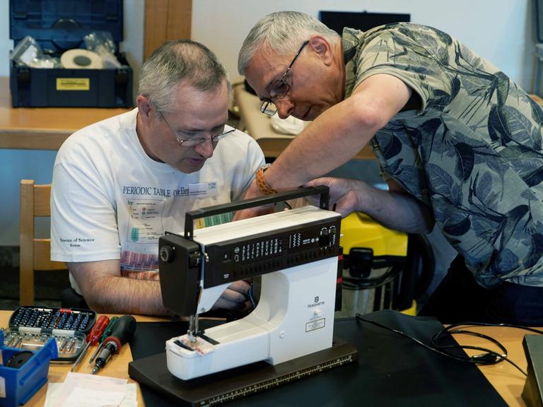 Zwei Mitarbeiter eines Repair-Cafes reparieren eine Nähmaschine.