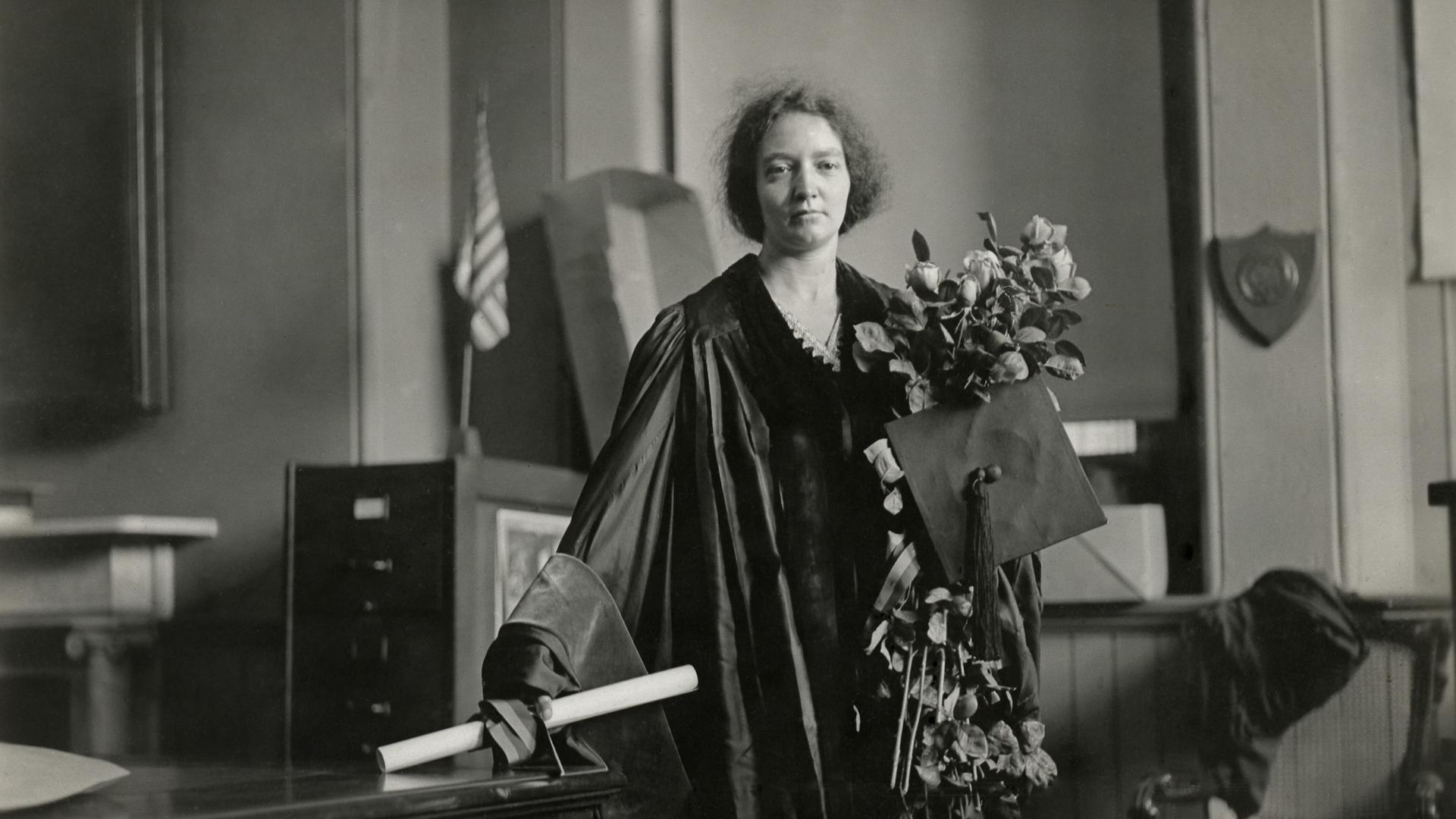 Die Physikerin Irene Joliot-Curie in akademischen Insignien: Sie trägt einen festlichen Talar, hält einen großen Blumenstrauß in der linken Hand und eine Schriftrolle in der rechten. Die Physikerin Irene Joliot-Curie in akademischen Insignien: Sie trägt einen festlichen Talar, hält einen großen Blumenstrauß in der linken Hand und eine Schriftrolle in der rechten.