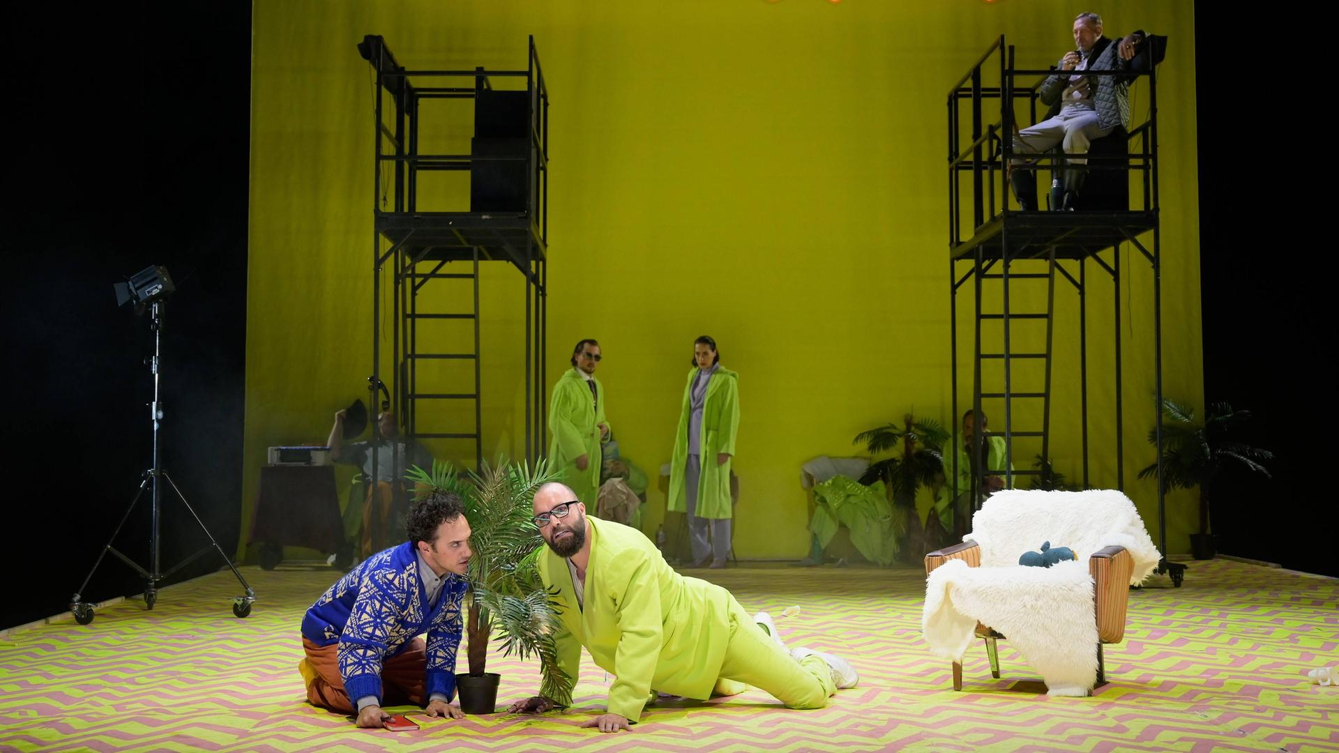 Auf einer Theaterbühne sind zwei Männer zu sehen. Sie befinden sich auf allen Vieren; zwischen ihnen steht eine Topfpflanze. Auf einer Theaterbühne sind zwei Männer zu sehen. Sie befinden sich auf allen Vieren; zwischen ihnen steht eine Topfpflanze.