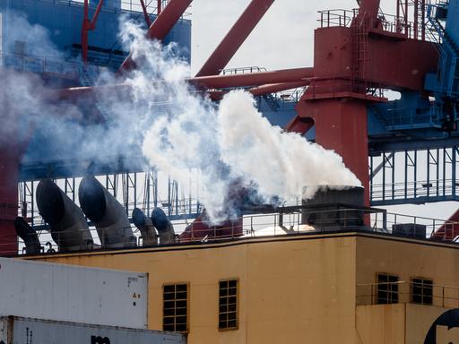 Abgase kommen aus dem Schornstein eines Containerschiffs, während es im Hamburger Hafen am Kai liegt und beladen wird.