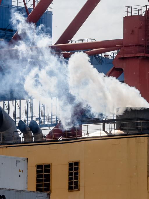 Abgase kommen aus dem Schornstein eines Containerschiffs, während es im Hamburger Hafen am Kai liegt und beladen wird.