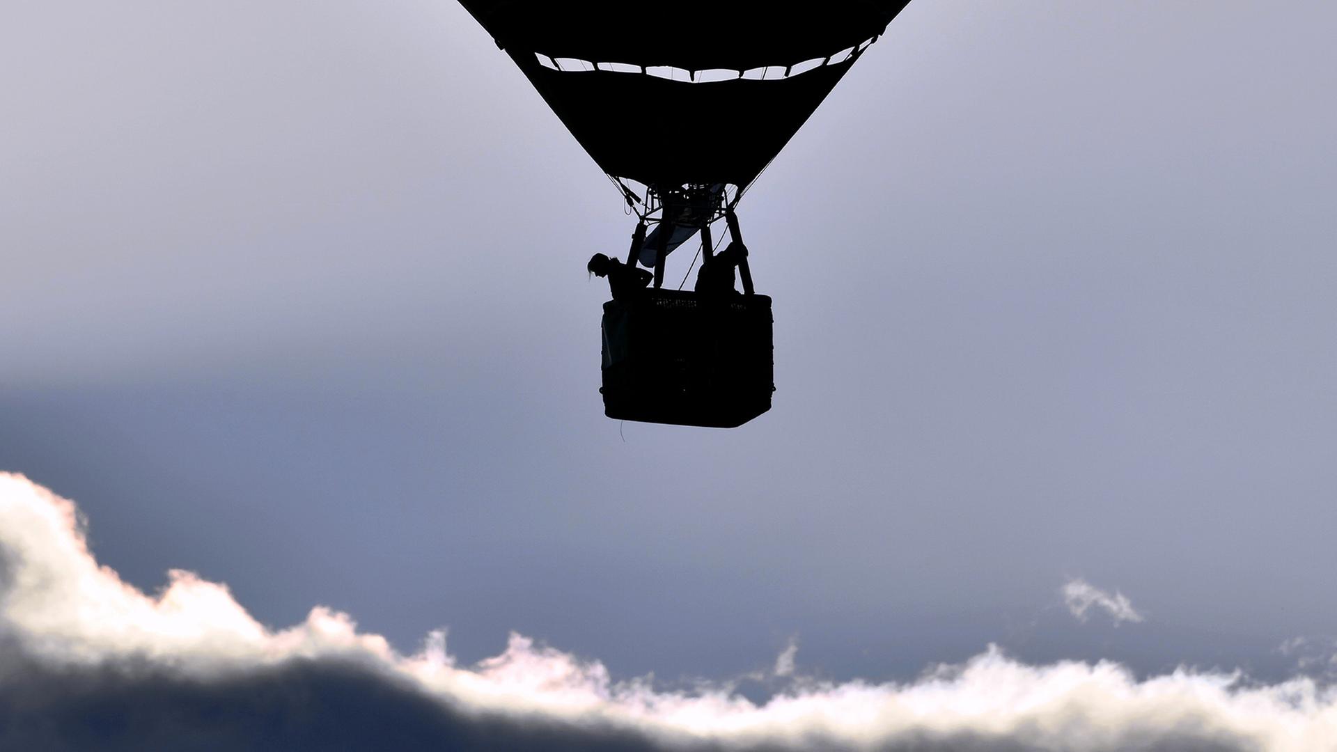 Ein Ballon mit Korb fährt über den Wolken.