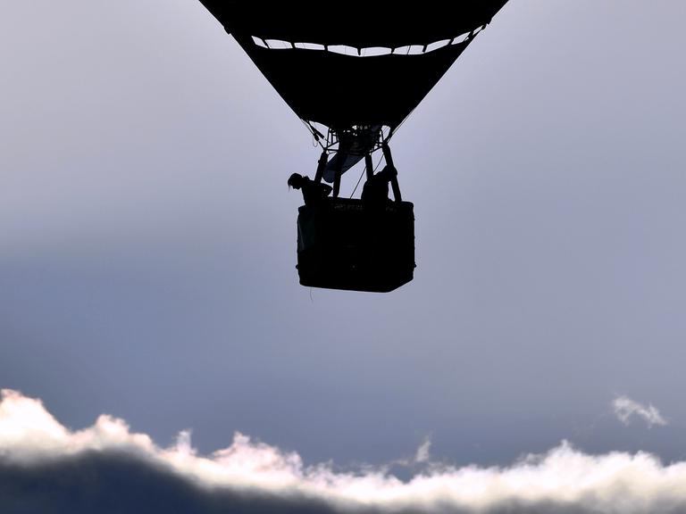 Ein Ballon mit Korb fährt über den Wolken.