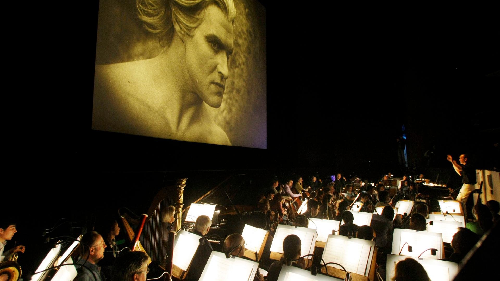 Musiker des HR-Sinfonieorchesters proben in einem abgedunkelten Raum. An einer Wand wird der Stummfilm "die Nibelungen" gezeigt. Musiker des HR-Sinfonieorchesters proben in einem abgedunkelten Raum. An einer Wand wird der Stummfilm "die Nibelungen" gezeigt.
