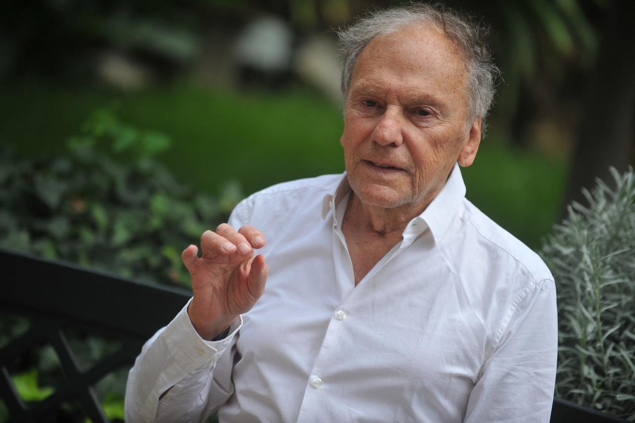 Jean-Louis Trintignant im Alter von etwa 80 Jahren auf einer Bank, im Hintergrund ist eine Parkanlage zu sehen. Er gestikuliert mit der rechten Hand. Jean-Louis Trintignant im Alter von etwa 80 Jahren auf einer Bank, im Hintergrund ist eine Parkanlage zu sehen. Er gestikuliert mit der rechten Hand.