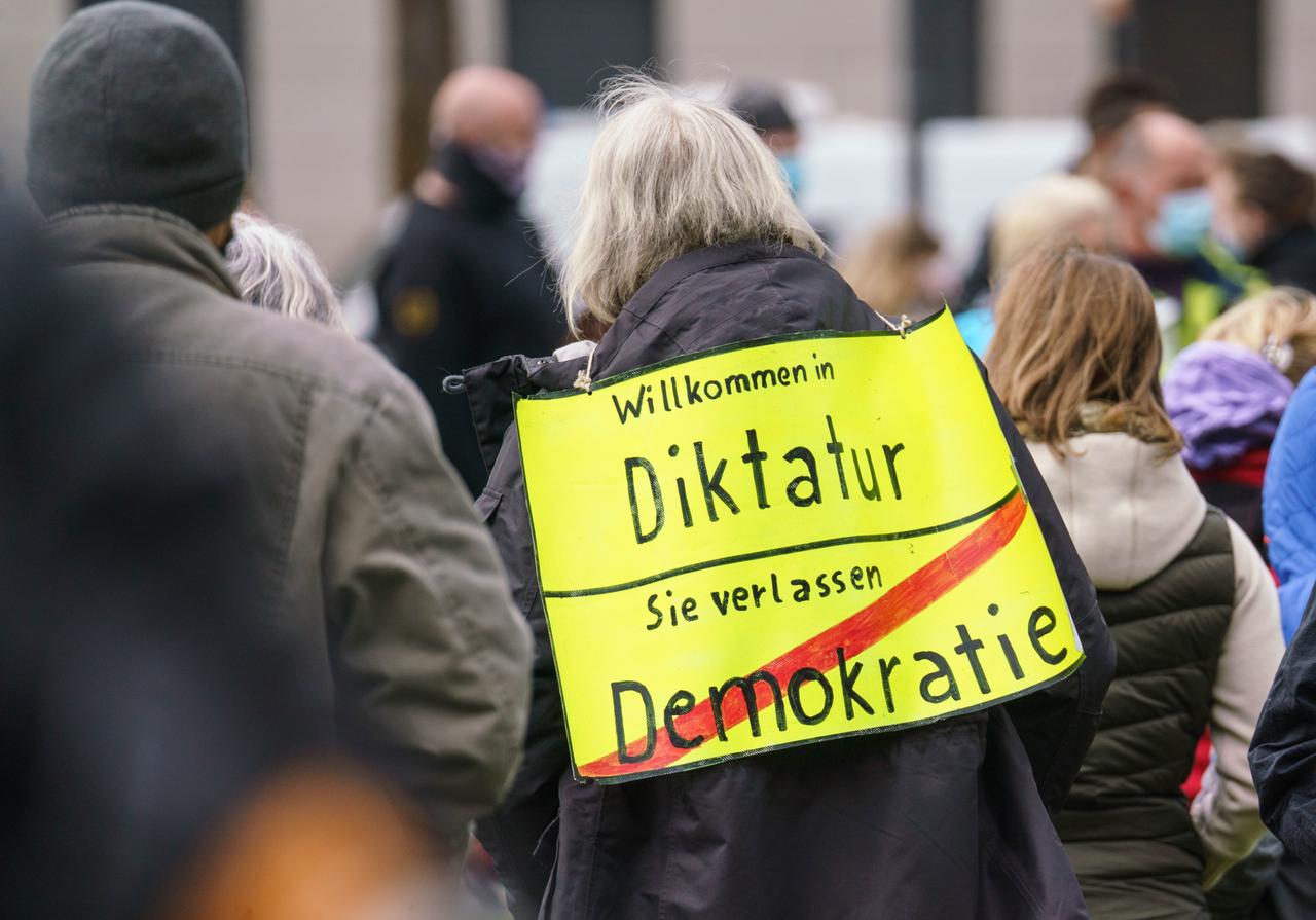 Eine Demonstrantin mit einem Plakat mit der Aufschrift "Willkommen in Diktatur - Sie verlassen Demokrati",, das einem Ortsschild nachempfunden ist. 