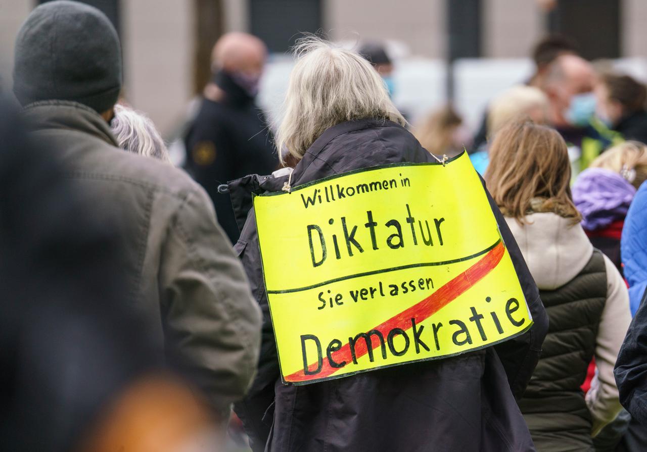 Eine Demonstrantin mit einem Plakat mit der Aufschrift "Willkommen in Diktatur - Sie verlassen Demokrati",, das einem Ortsschild nachempfunden ist. Eine Demonstrantin mit einem Plakat mit der Aufschrift "Willkommen in Diktatur - Sie verlassen Demokrati",, das einem Ortsschild nachempfunden ist.