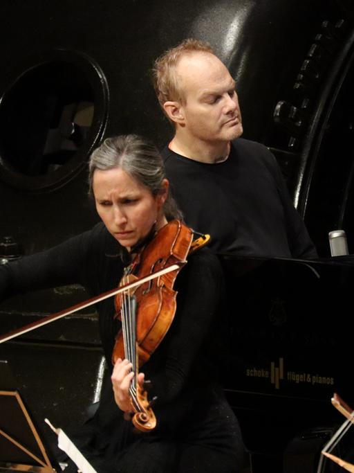 Eine Bratschistin, ein Pianist und eine Cellistin musizieren auf einer Bühne. Im Hintergrund sind Maschinen des Jugendstil-Kraftwerks Heimbach (Eifel)  zu sehen.