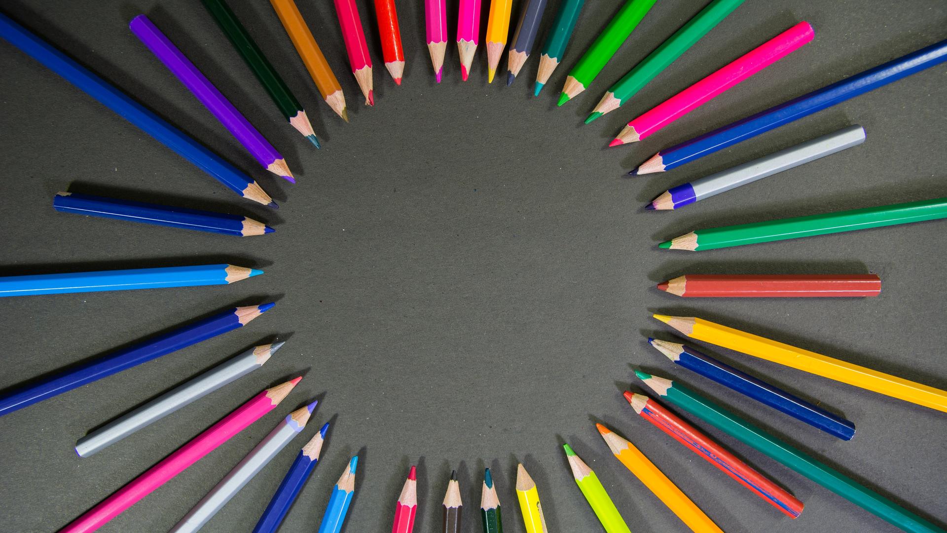 Viele bunte Stifte liegen auf einem grauen Hintergrund aufgefächert Viele bunte Stifte liegen auf einem grauen Hintergrund aufgefächert