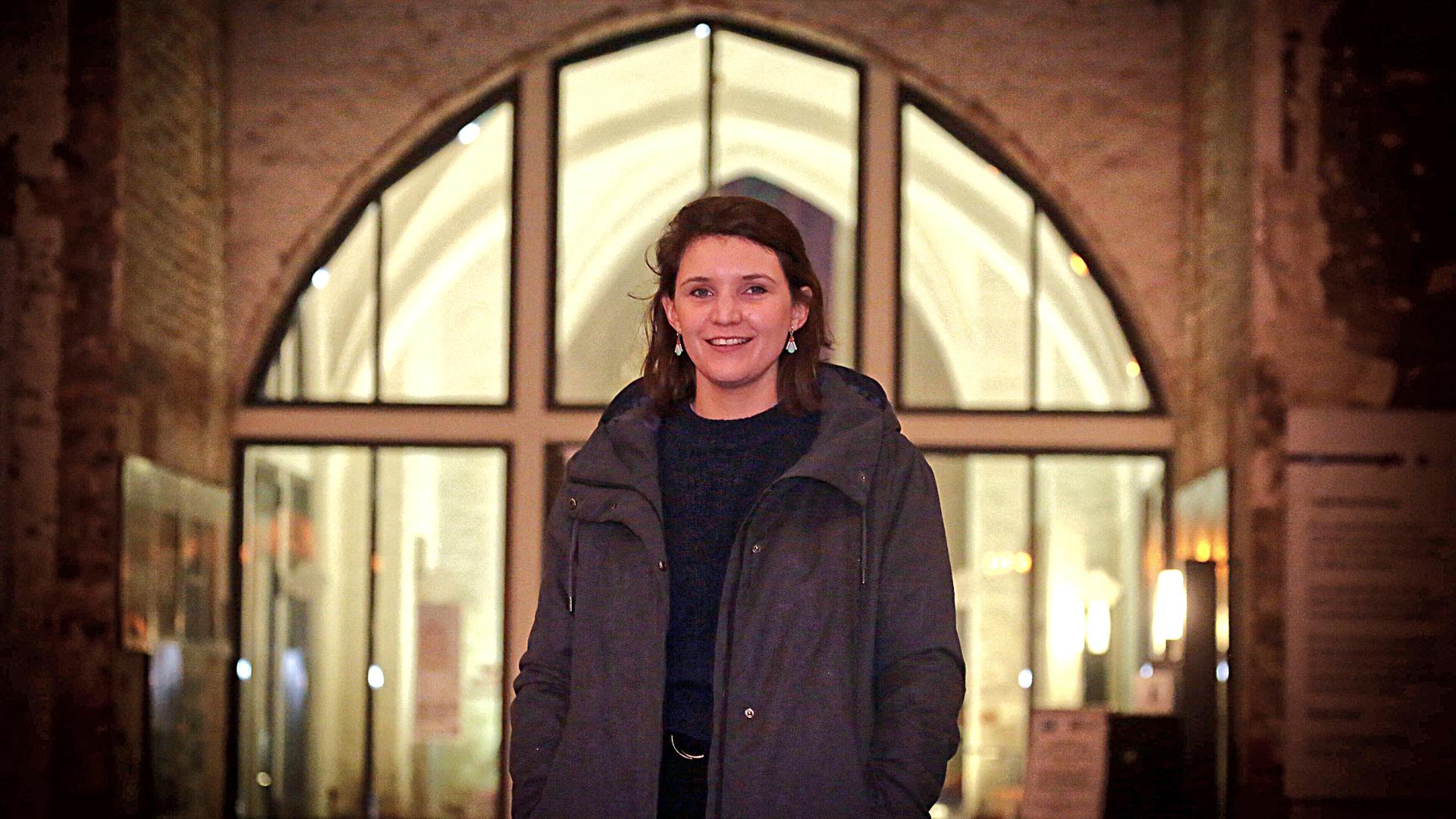 Verena Keßler steht in dunkler Jacke vor einem großen erleuchteten Fenster. Verena Keßler steht in dunkler Jacke vor einem großen erleuchteten Fenster.