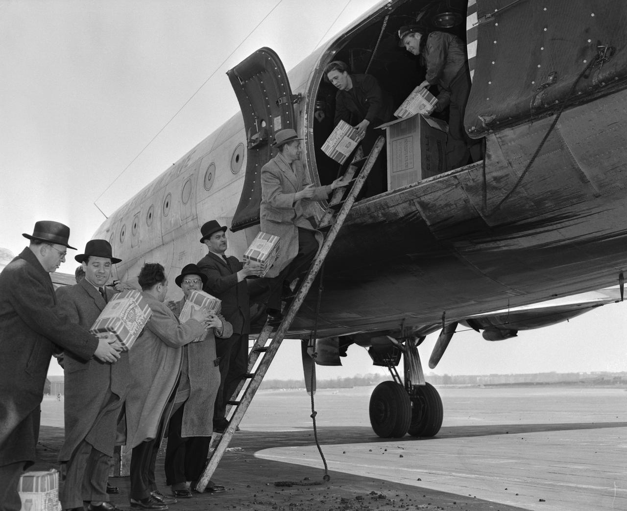 Historisches Schwarz-Weiß-Foto mehrerer Männer, die Pakete aus einem Flugzeug räumen und per Menschenkette weiterreichen. Historisches Schwarz-Weiß-Foto mehrerer Männer, die Pakete aus einem Flugzeug räumen und per Menschenkette weiterreichen.