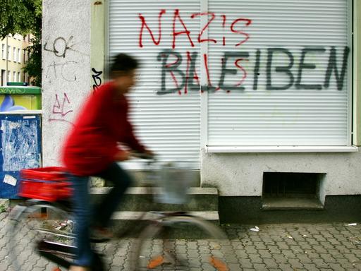 Eine Geschäftsfront ist mit dem roten Schriftzug "NAZIS RAUS", besprüht. Darüber hat jemand in Schwarz "BLEIBEN" geschrieben.