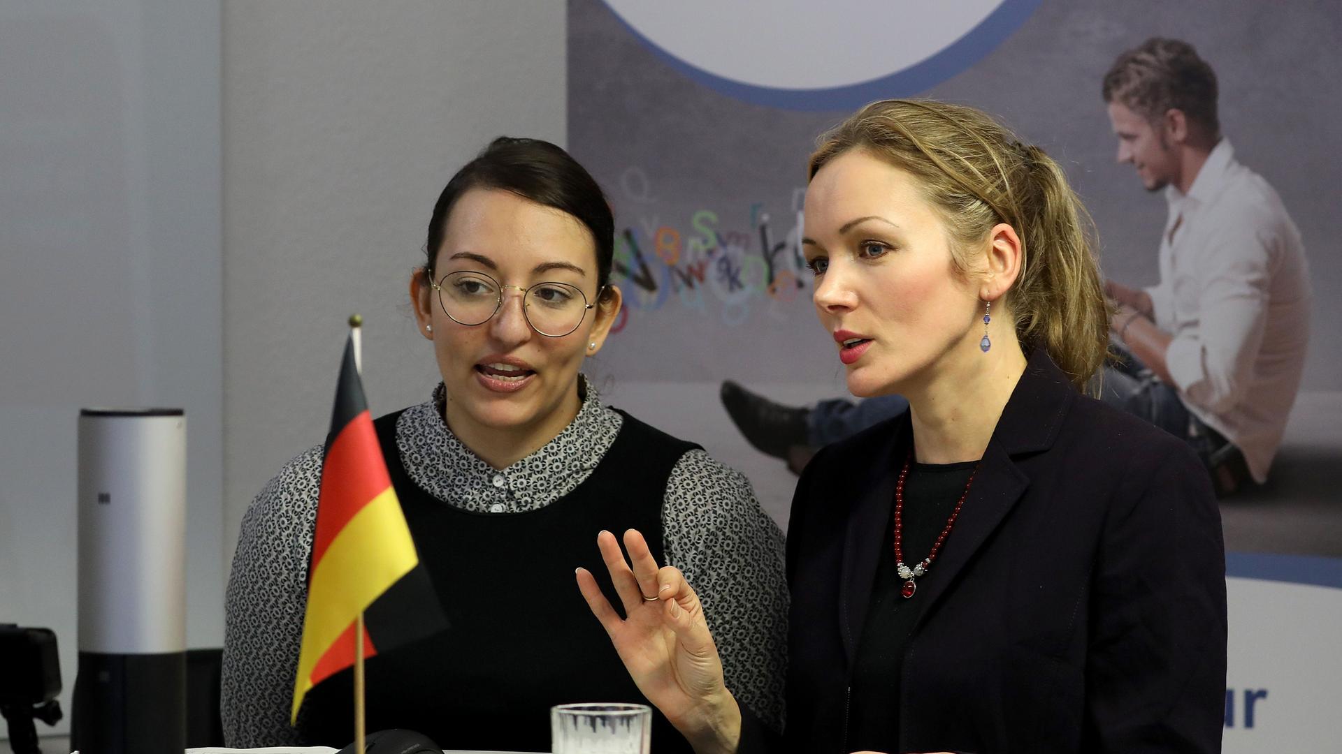 Shirin Fummel (l), und Jeanette von Zelewski, Mitarbeiter der Zentralen Servicestelle Berufsanerkennung bei der Zentralen Auslands- und Fachvermittlung (ZAV), sprechen während eines Online-Chats mit ausländischen Fachkräften. Die jungen Frauen stehen an einem kreisrunden Stehtisch, auf dem eine kleine Deustchland-Flagge steht. Shirin Fummel (l), und Jeanette von Zelewski, Mitarbeiter der Zentralen Servicestelle Berufsanerkennung bei der Zentralen Auslands- und Fachvermittlung (ZAV), sprechen während eines Online-Chats mit ausländischen Fachkräften. Die jungen Frauen stehen an einem kreisrunden Stehtisch, auf dem eine kleine Deustchland-Flagge steht.
