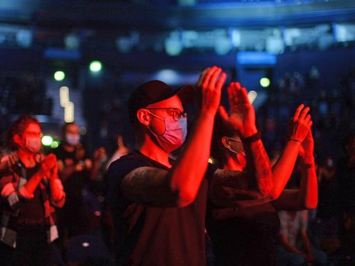 Stehendes Publikum mit Schutzmasken und in rot getauchtes Licht, auf einem Idoor-Konzert der Band "Madsen" in Hamburg.