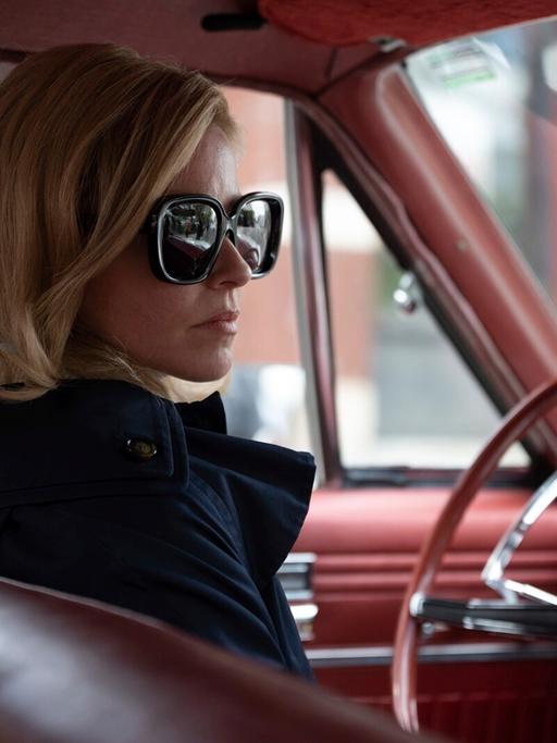 Elizabeth Banks mit Sonnenbrille sitzt am Steuer eines alten amerikanischen Straßenkreuzers.