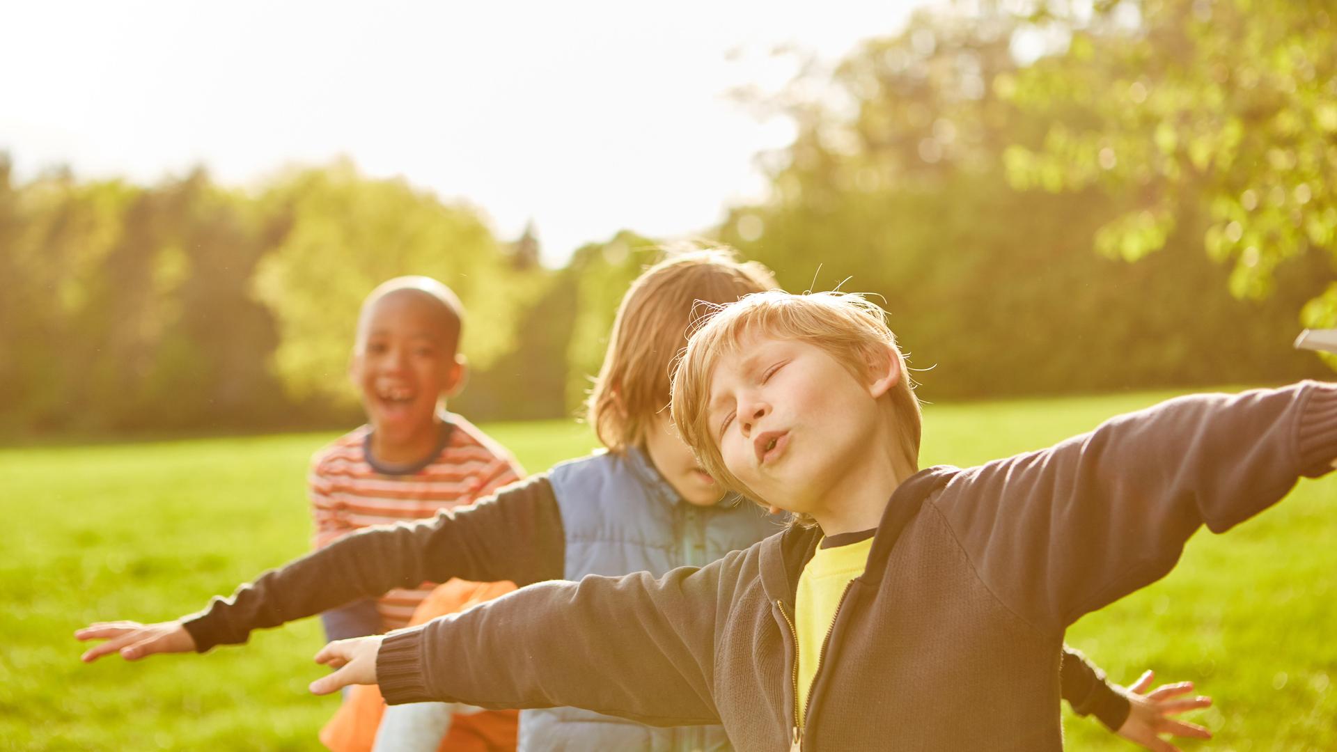 Gruppe Kinder im Park mit ausgebreiteten Armen spielt Fliegen auf dem Kindergeburtstag Gruppe Kinder im Park mit ausgebreiteten Armen spielt Fliegen auf dem Kindergeburtstag