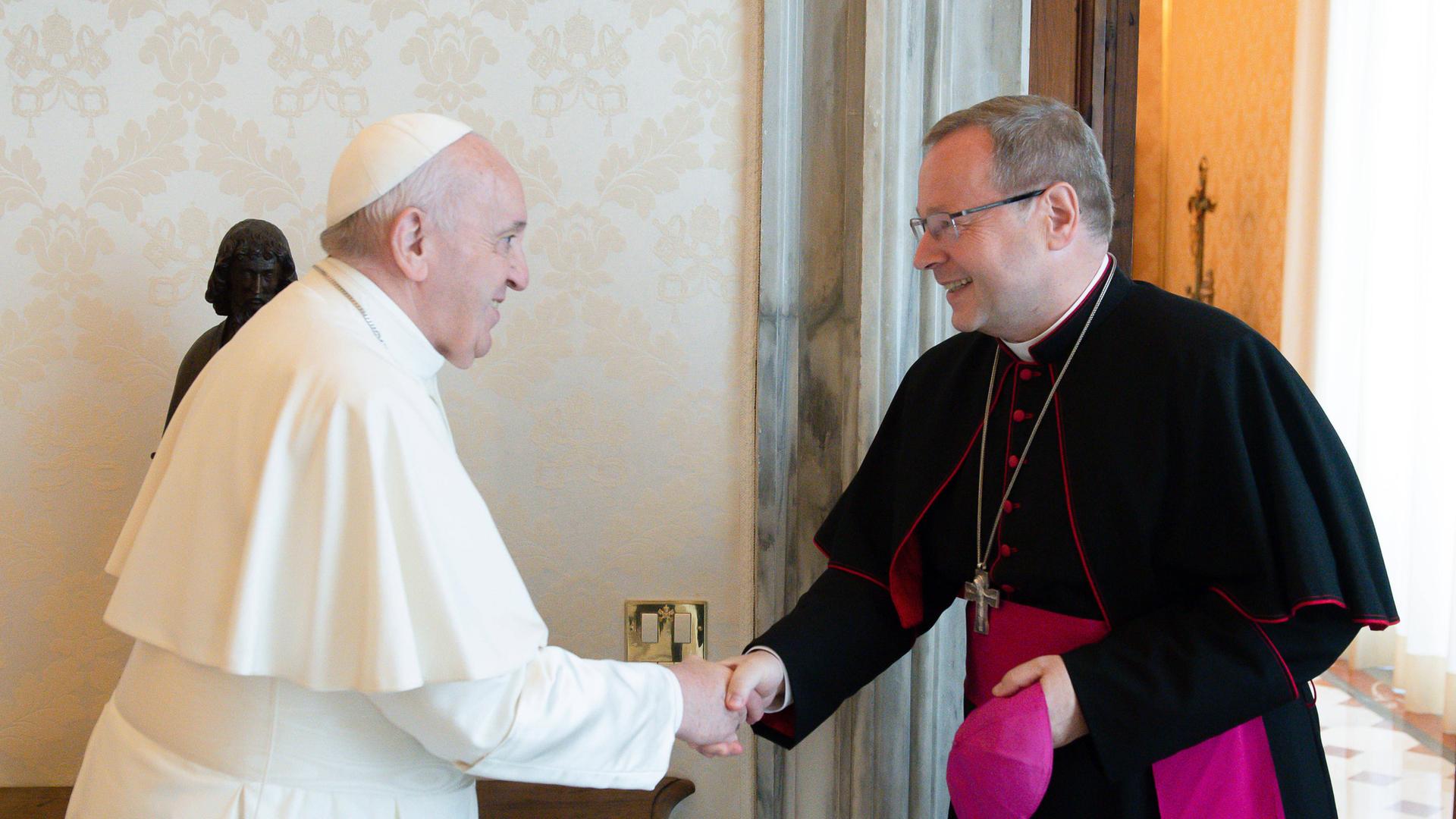 Papst Franziskus schüttelt die Hand von Georg Bätzing, dem Vorsitzenden der Deutschen Bischofskonferenz. Bätzing hat seine Kappe abgenommen, beide lächeln. Papst Franziskus schüttelt die Hand von Georg Bätzing, dem Vorsitzenden der Deutschen Bischofskonferenz. Bätzing hat seine Kappe abgenommen, beide lächeln.