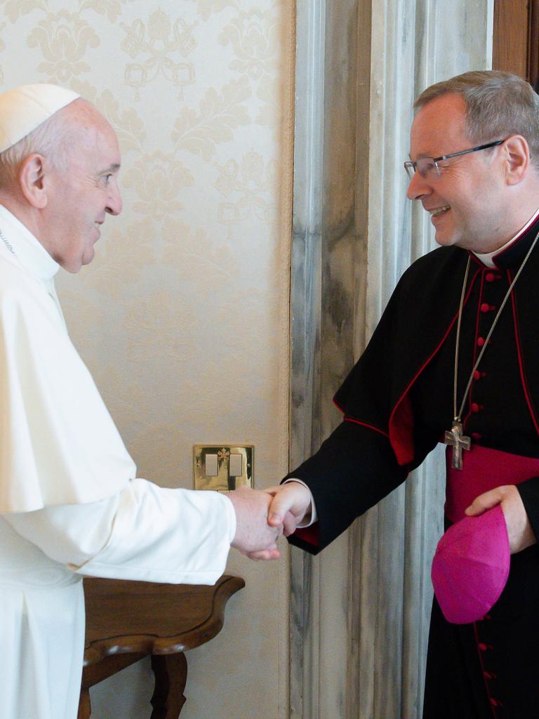 Papst Franziskus schüttelt die Hand von Georg Bätzing, dem Vorsitzenden der Deutschen Bischofskonferenz. Bätzing hat seine Kappe abgenommen, beide lächeln.