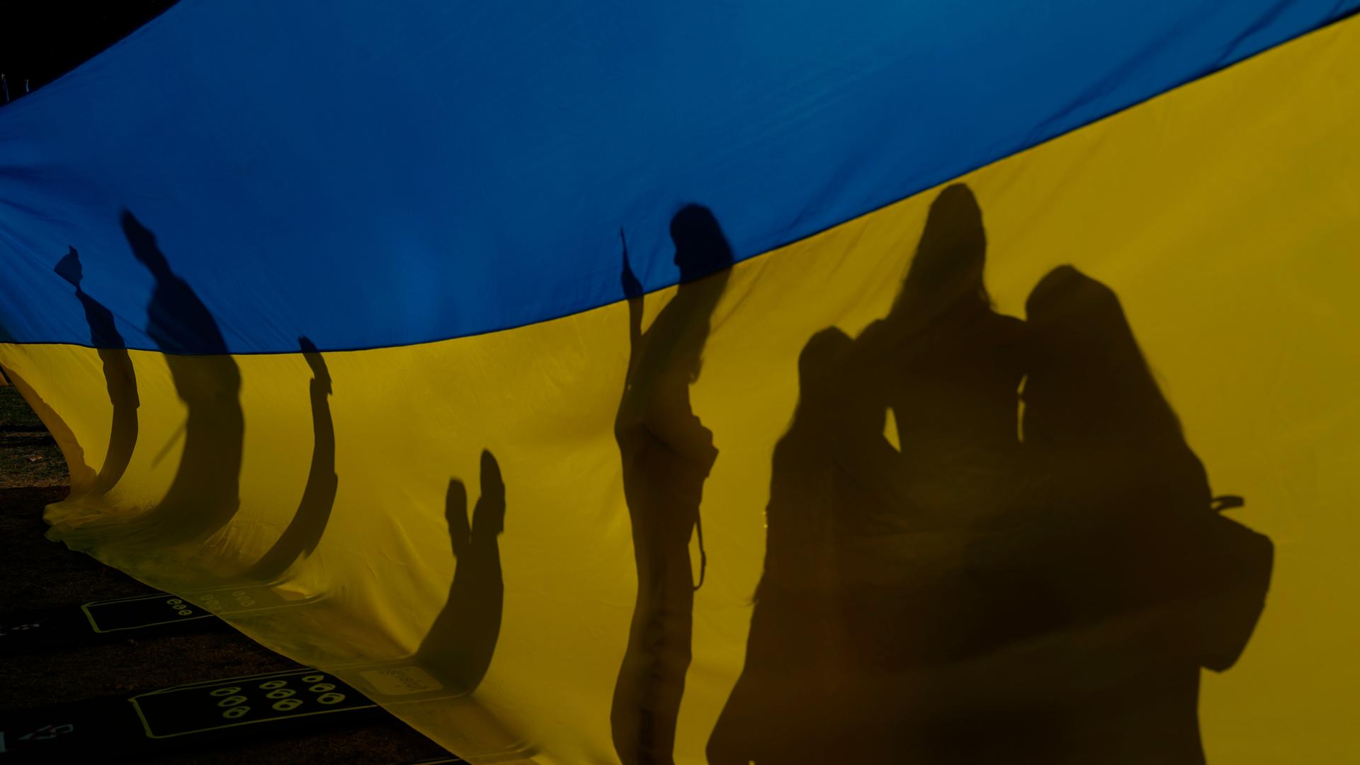 Schattenrisse von eine Gruppe von Menschen hinter einer großen blau-gelben ukrainischen Fahne. Schattenrisse von eine Gruppe von Menschen hinter einer großen blau-gelben ukrainischen Fahne.