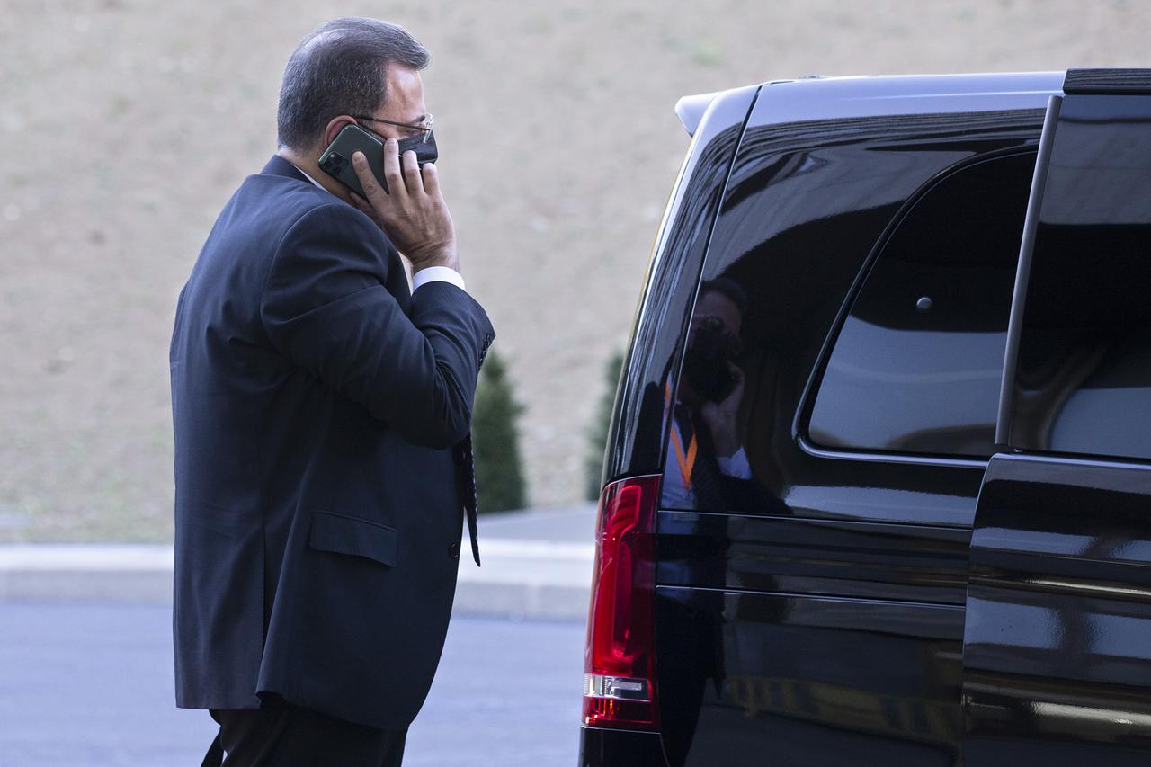 A man in a suit on the phone next to a black car stands: Ahmad Kuzbari, member of the Syrian government and co-chair of the constitutional committee.